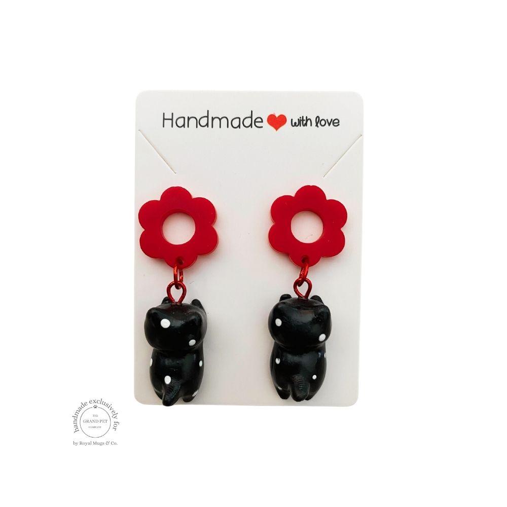 A pair of handcrafted polymer clay earrings in the shape of a black and white dotted cat with a red flower, displayed on a white backing card with 'HANDMADE WITH LOVE' text.