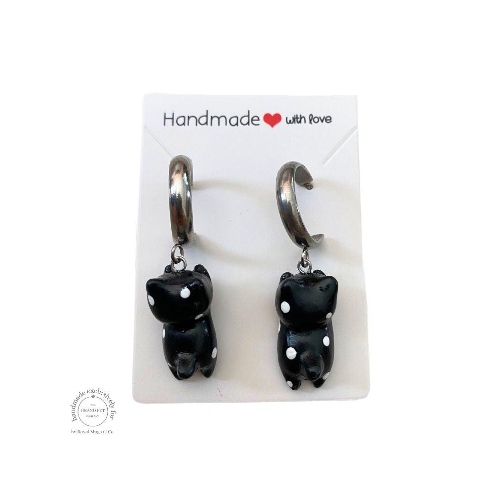 A pair of handcrafted polymer clay earrings in the shape of a black and white dotted cat with silver hoops, packaged on a card with 'Handmade with love' text.