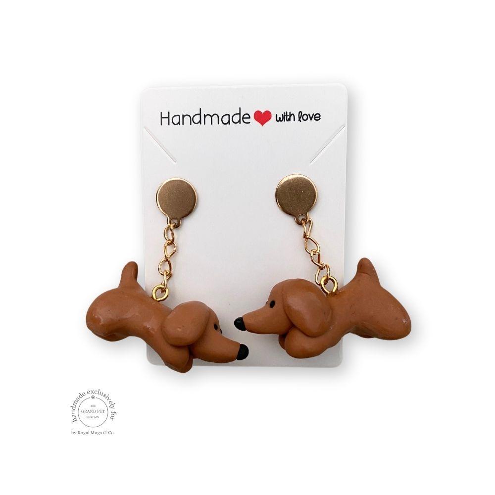 A pair of brown polymer clay earrings in the shape of dogs with brown stud, displayed on a white backing card with 'handmade with love' text.