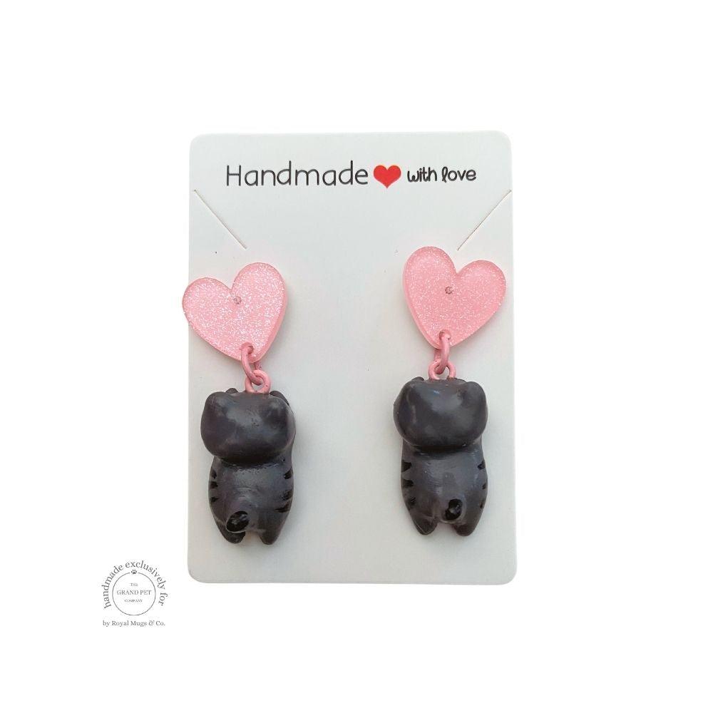 A pair of handcrafted grey polymer clay earrings with light pink glitter hearts, displayed on a white card with 'HANDMADE WITH LOVE' text.