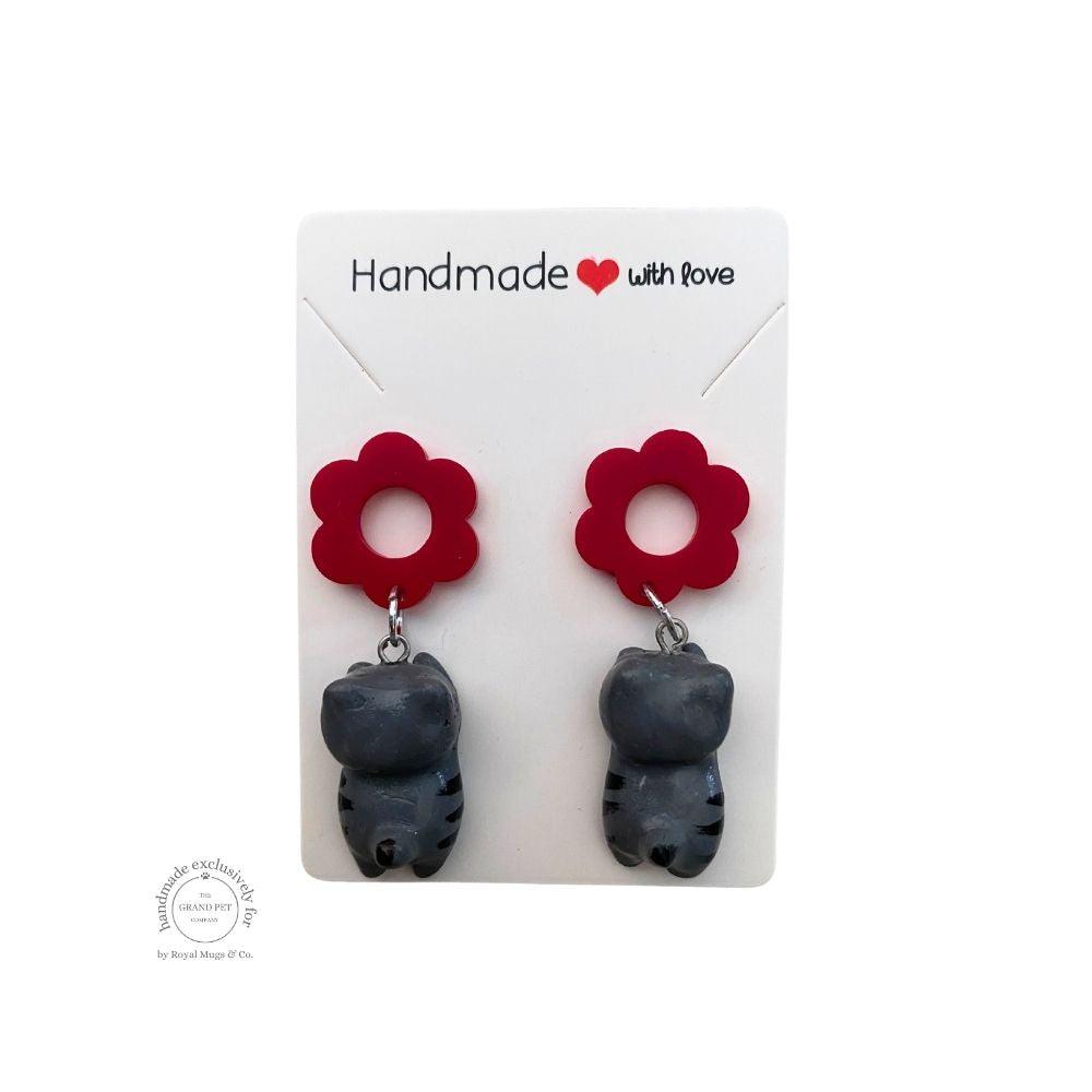 A pair of handcrafted polymer clay earrings in the shape of a cat with red flower details, presented on a white backing card with 'HANDMADE WITH LOVE' text.