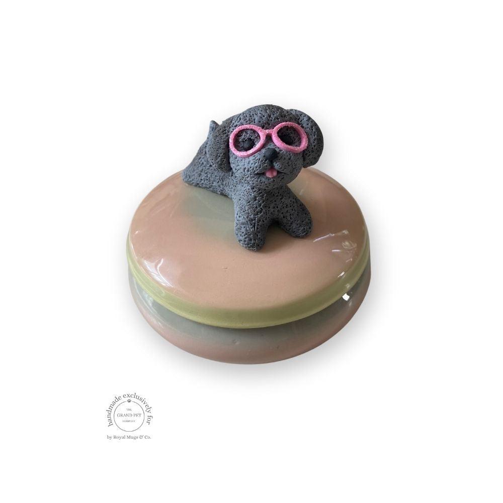 A round trinket tin with a sculpted grey poodle wearing sunglasses on top, set on a beige background.