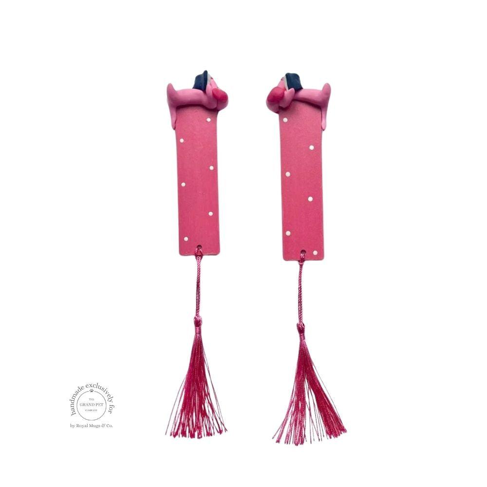 A pink polka dot bookmark with a sniffing dachshund lying on top and a pink hanging tassel