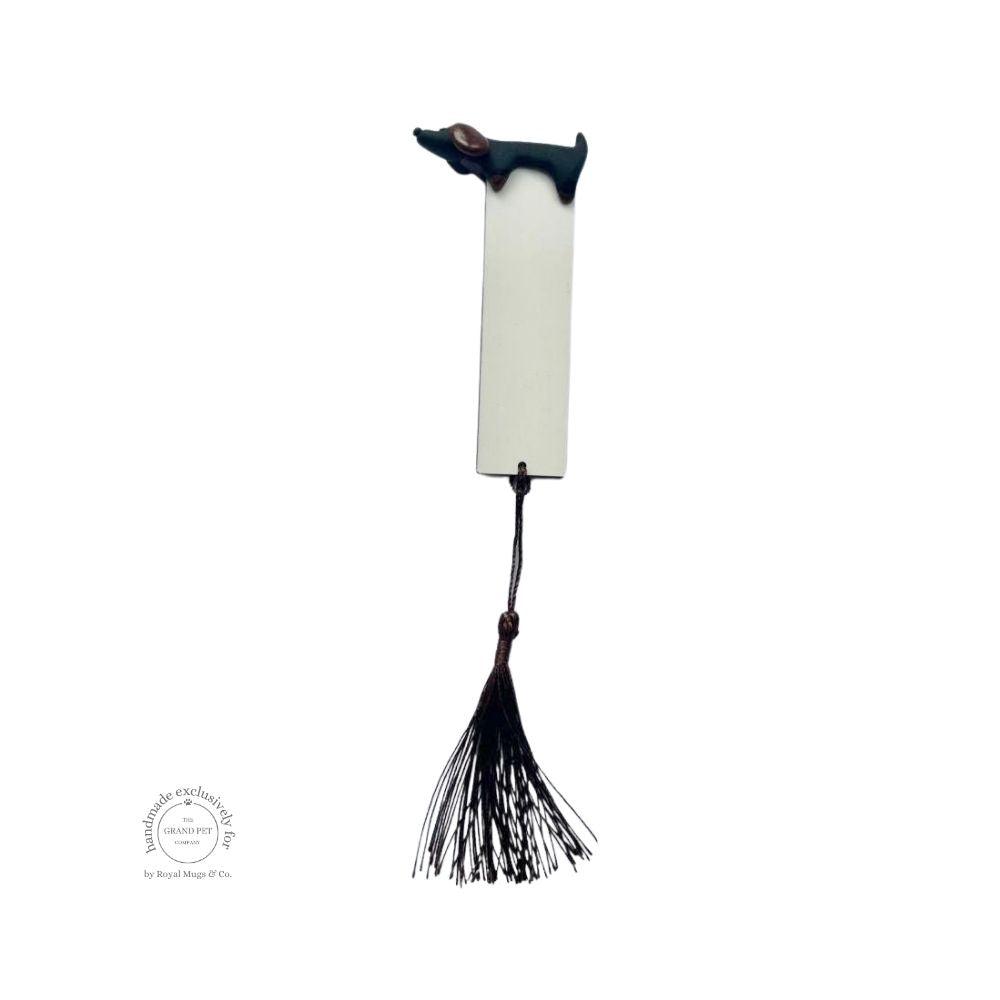 A white bookmark with a sniffing dachshund lying on top and a black hanging tassel