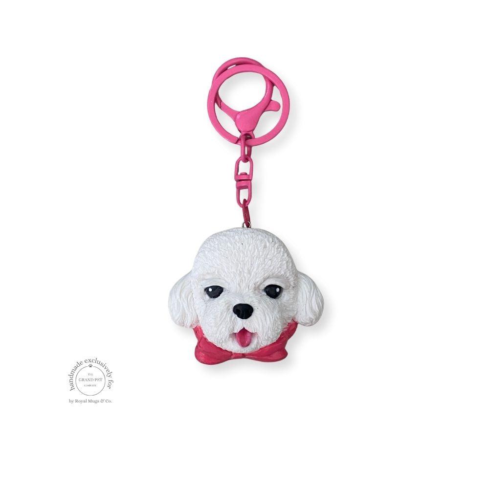 A hand-sculpted keychain in the likeness of a white poodle with a pink bow, made from premium FIMO polymer clay.
