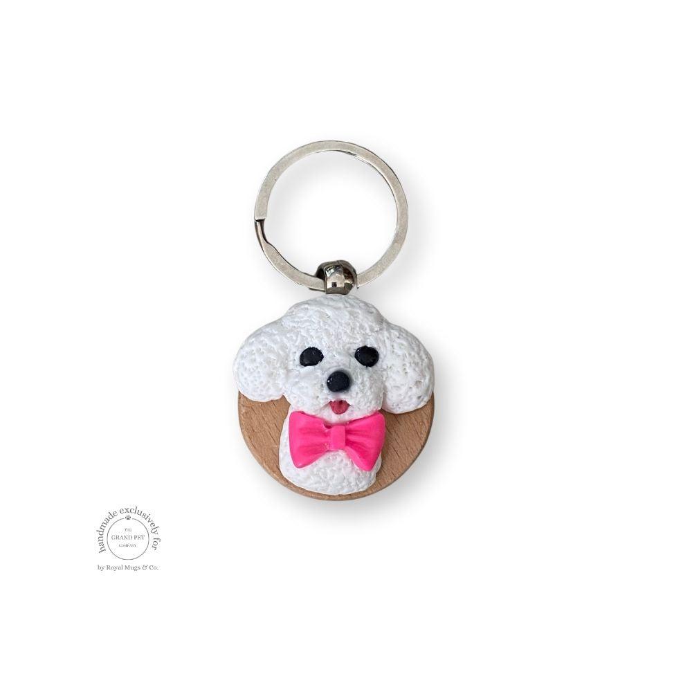 A hand-sculpted keychain depicting a white poodle with a pink bow, made from polymer clay.