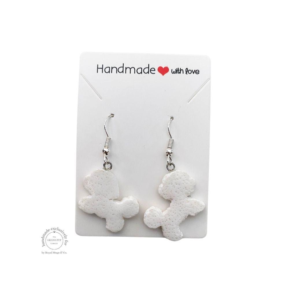 A pair of white polymer clay earrings in the shape of a poodle with silver hoops, displayed on a white backing card with 'handmade with love' text.