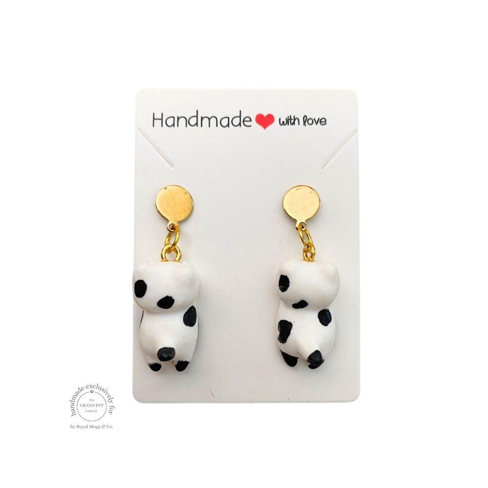 A pair of handcrafted polymer clay earrings in the shape of a white and black cat with gold circles, packaged on a card with 'HANDMADE WITH LOVE' text.