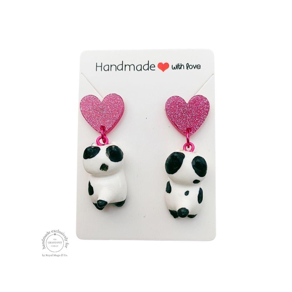 A pair of handcrafted polymer clay earrings in the shape of a white and black cat with pink glitter hearts, displayed on a clear plastic card with 'HANDMADE WITH LOVE' text.