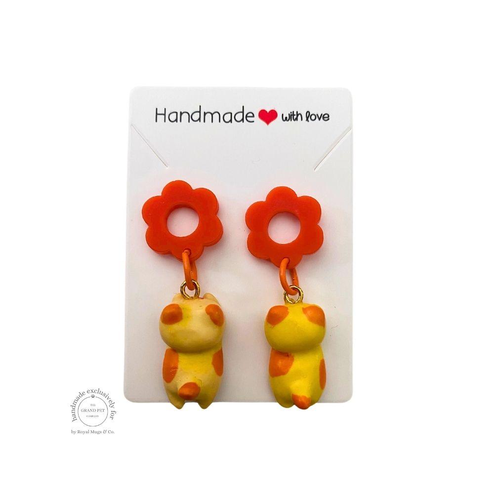 A pair of yellow polka polymer clay earrings in the shape of cats with orange flower, displayed on a white backing card with 'handmade with love' text.