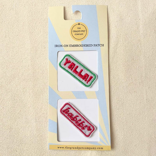 Two colourful iron on embroidered felt patches with fun Arabic expressions on packaging with 'The Grand Pet Company' branding.