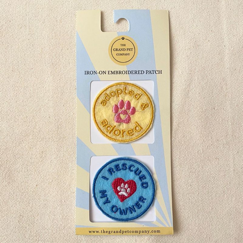 Two blue and yellow rescue themed iron on felt embroidered felt patches on packaging with 'The Grand Pet Company' branding.