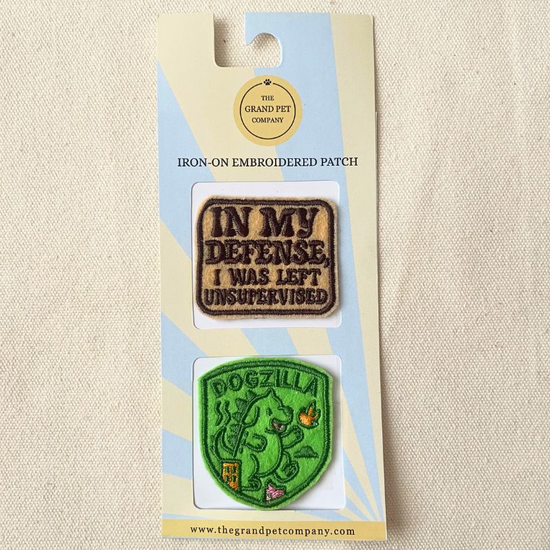 Two fun and cheeky iron on felt embroidered patches on packaging with 'The Grand Pet Company' branding.