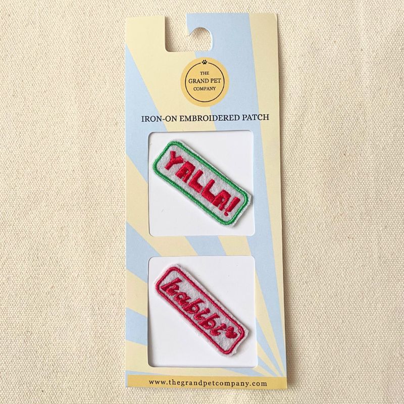 Two colourful iron on embroidered felt patches with fun Arabic expressions on packaging with 'The Grand Pet Company' branding.