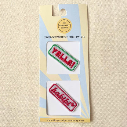 Two colourful iron on embroidered felt patches with fun Arabic expressions on packaging with 'The Grand Pet Company' branding.
