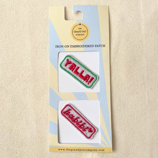 Two colourful iron on embroidered felt patches with fun Arabic expressions on packaging with 'The Grand Pet Company' branding.